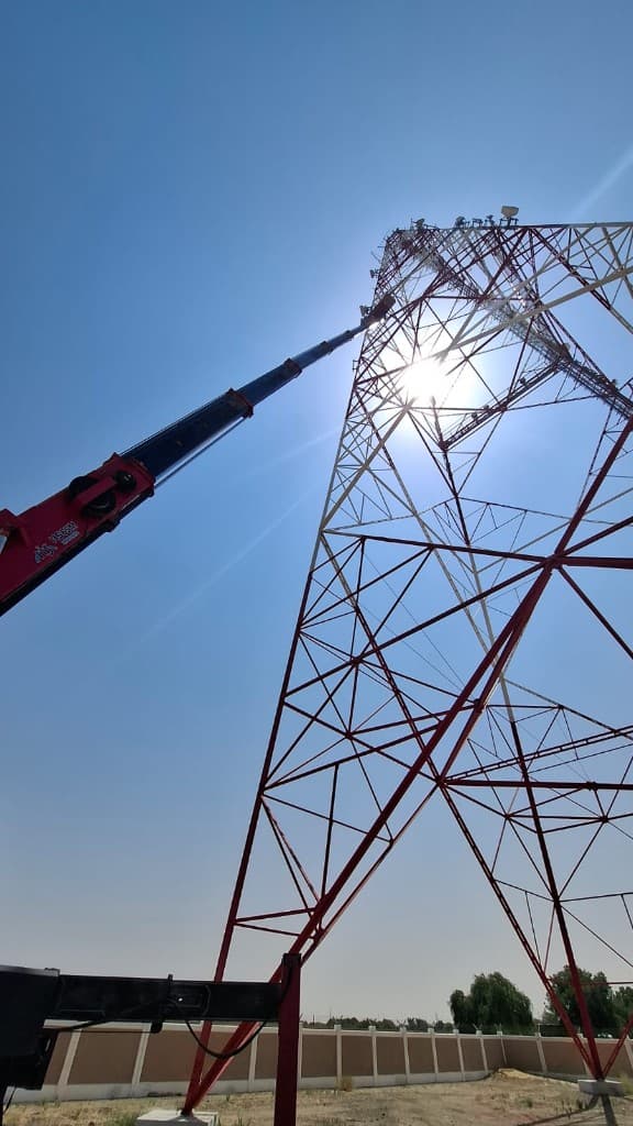 Truck-mounted manlift set up on a compound next to a lattice tower